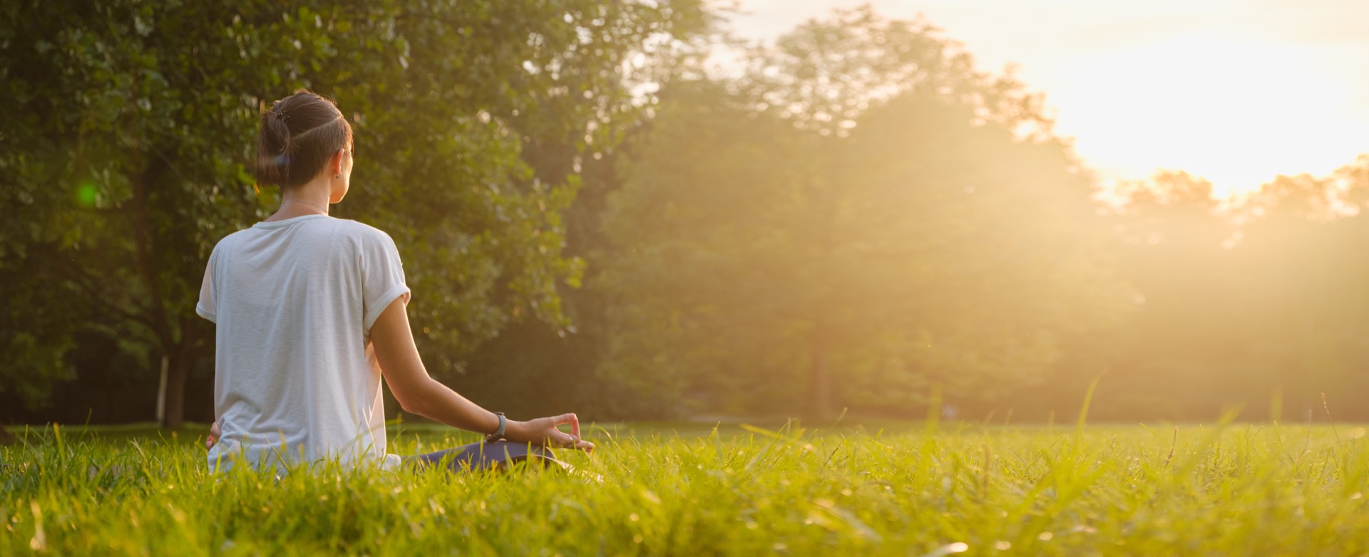 Mujer sentada en calma sobre la hierba al atardecer